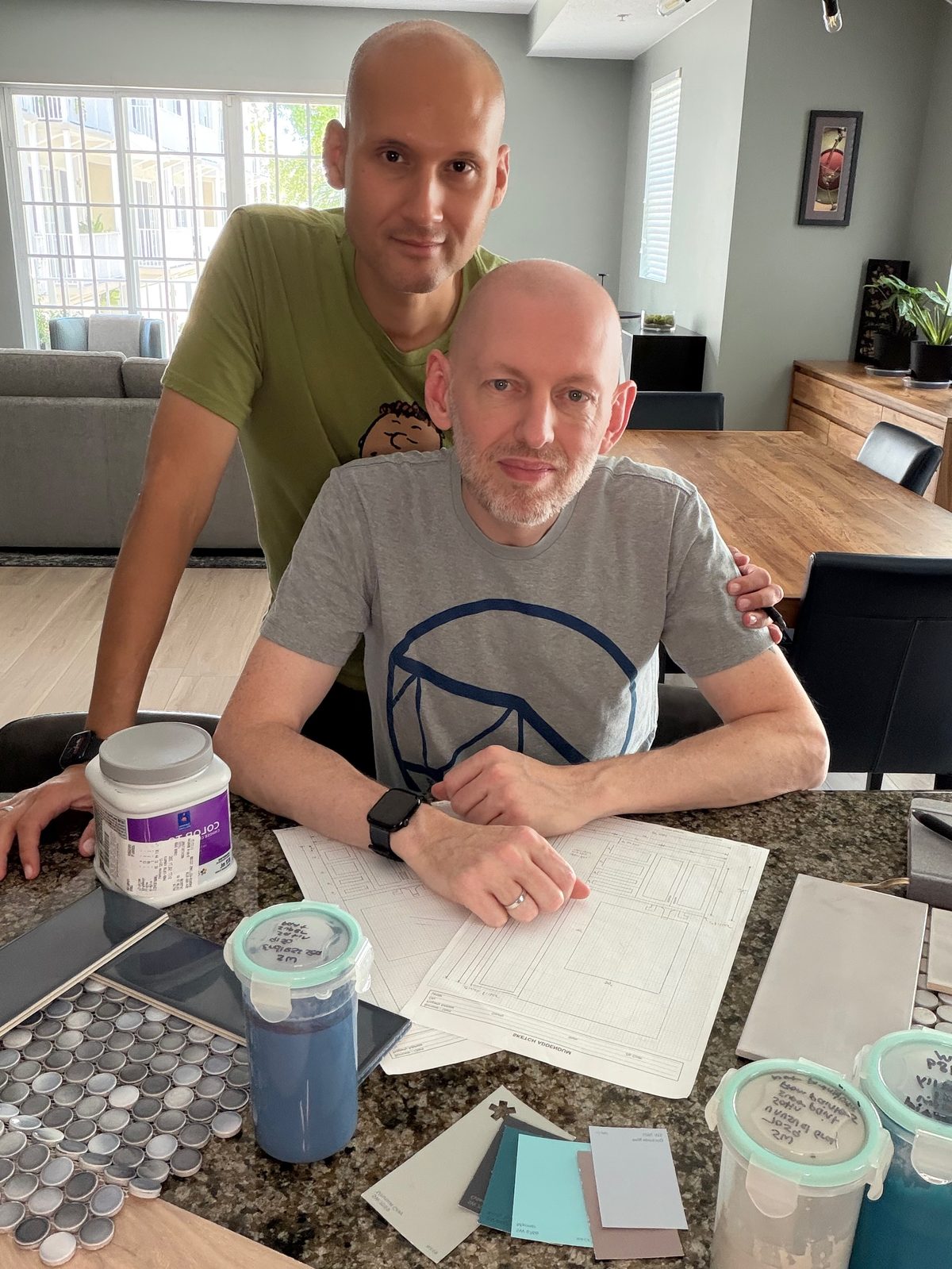 Daniel and his husband at the kitchen counter with renovation plans and tile samples